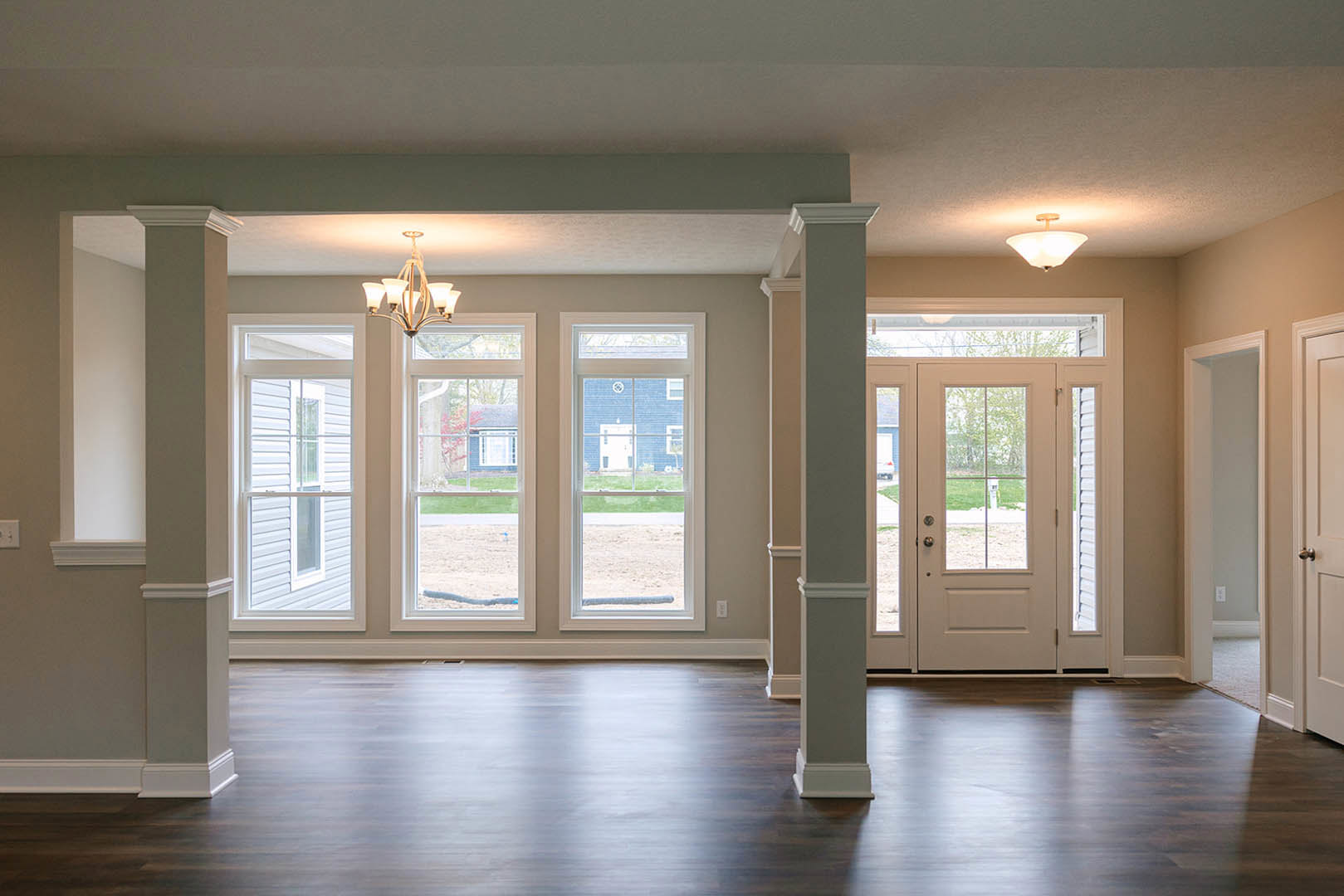 Hardwood floor with white walls, white door featuring glass panes, large window showing blue building outside, close-up of modern light fixture, white trim and molding