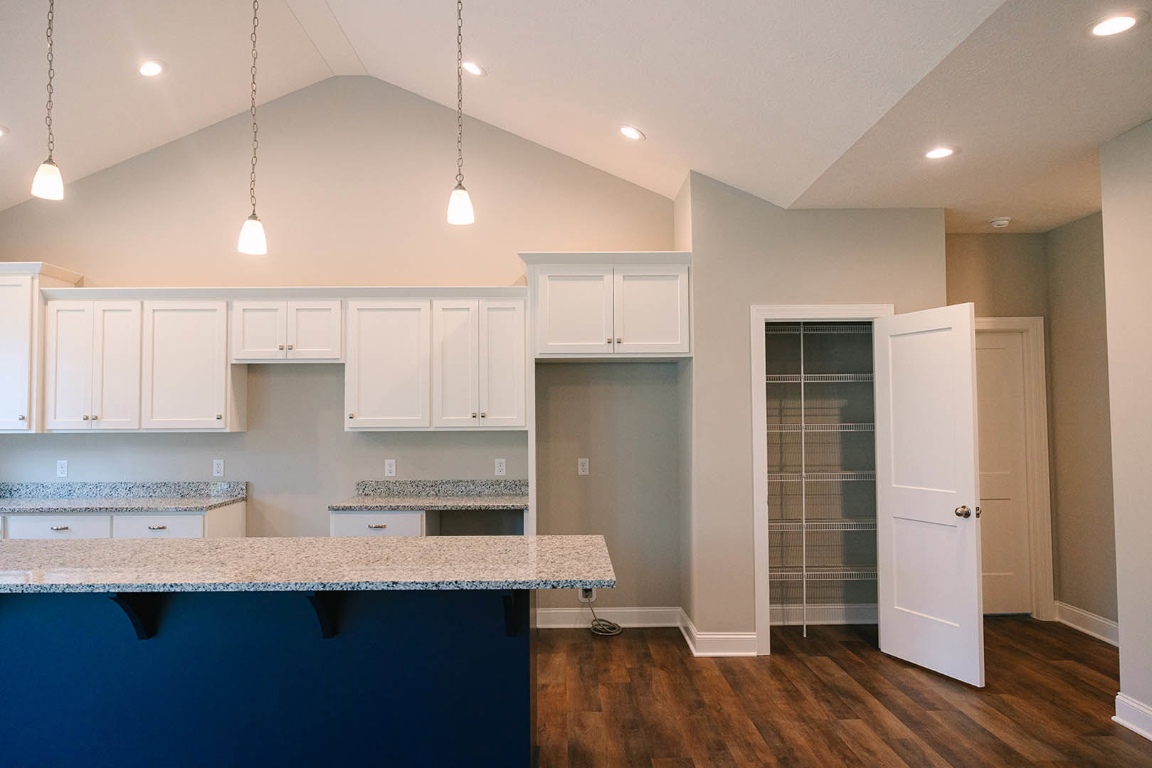 Marble kitchen island with white cabinetry, stainless steel sink, wood flooring, and blue accent wall