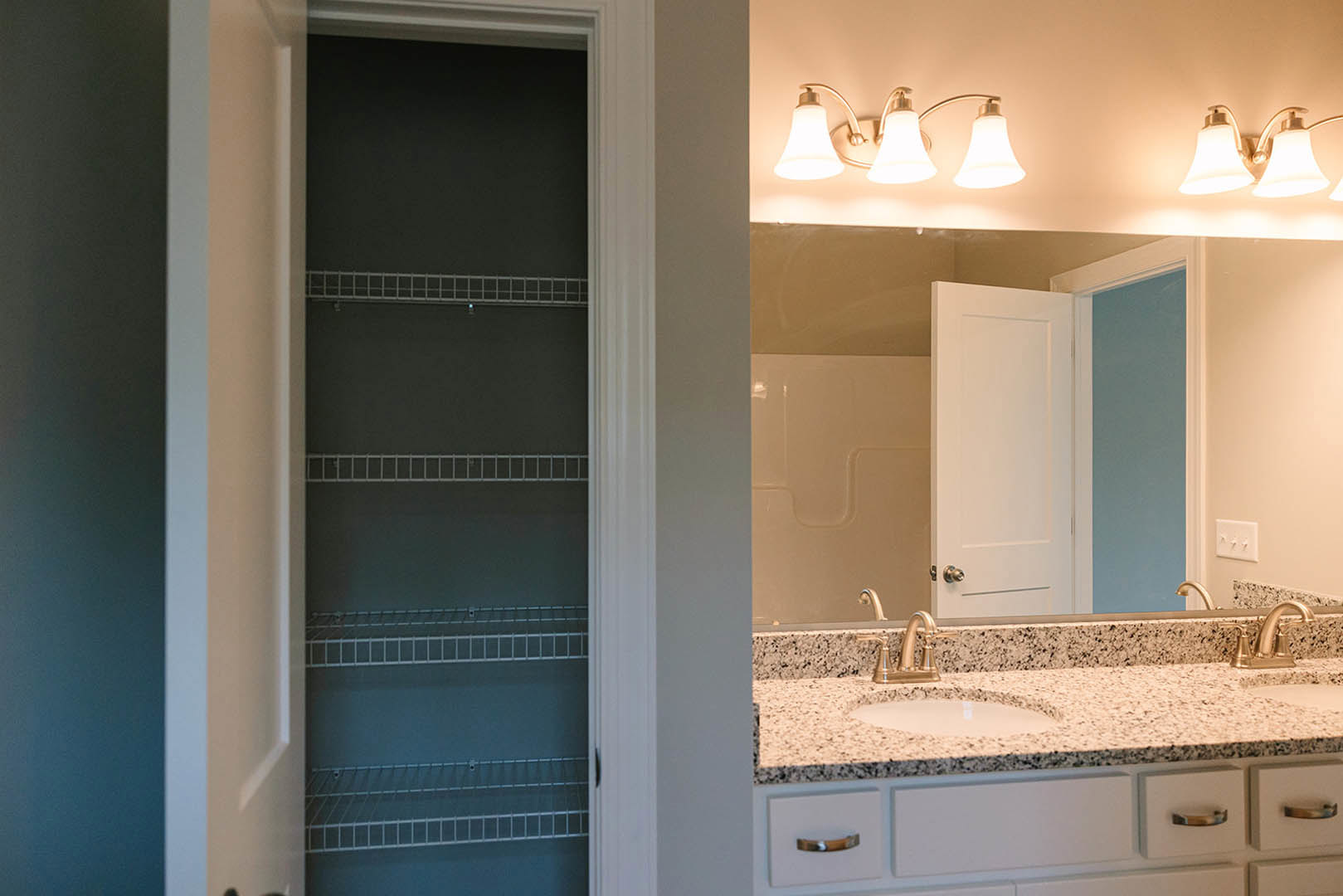 Bathroom with white tile walls, rectangular sink set in a light wood vanity, black faucet, large frameless mirror, and built-in shelving visible in the background.