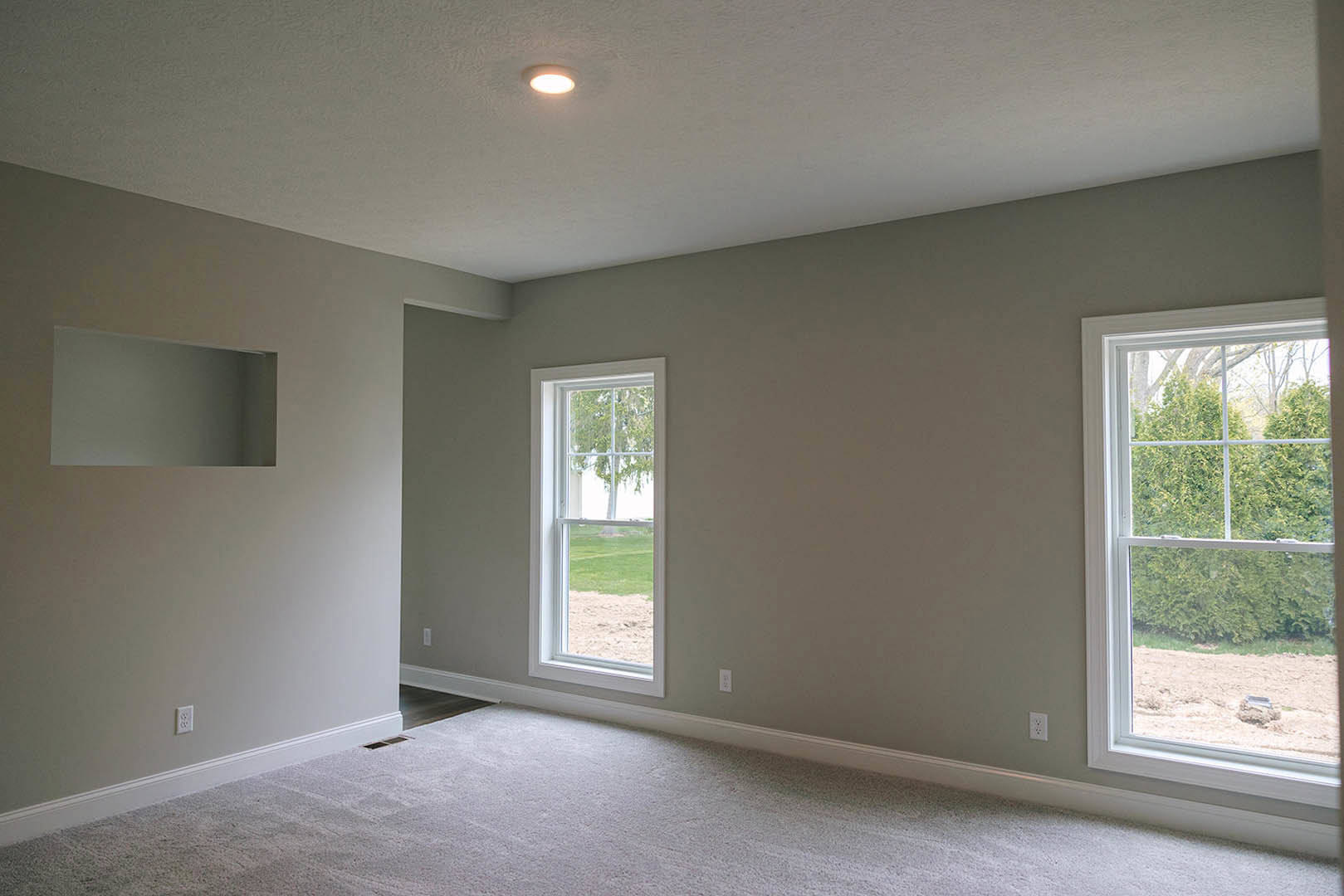 Carpeted room with large windows overlooking lawn and trees, white walls, ceiling light fixture