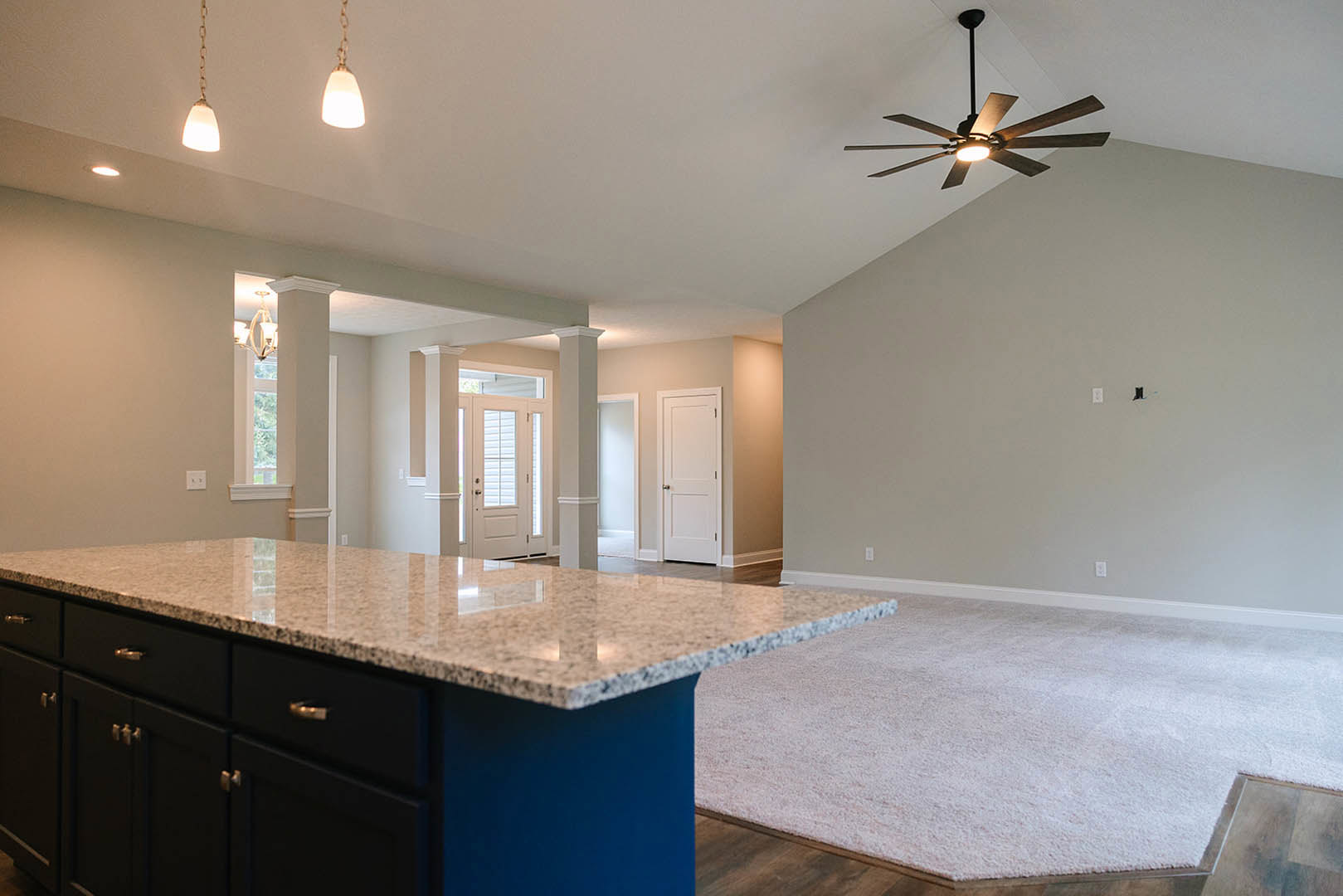 Marble kitchen island with dark cabinetry, stainless steel drawer handles, white door with blinds, ceiling fan with light fixture, carpeted adjacent room, neutral walls and modern