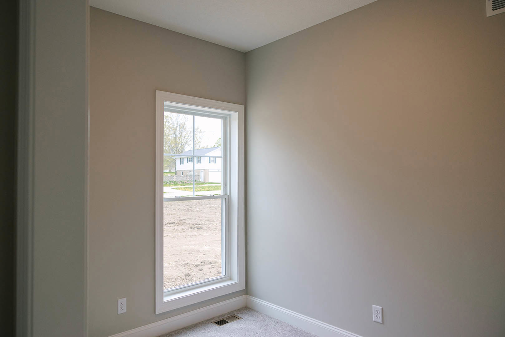 White plaster walls with crown molding, large window with blinds, wood floor, ceiling vent, and view of neighboring house through the window