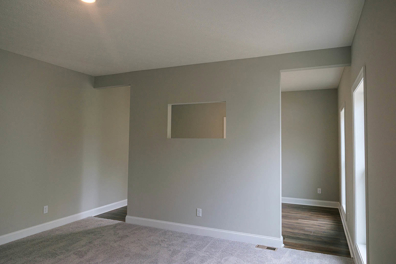 Bright room with large window, wood flooring, white ceiling, gray walls, wall mirror, and carpet accent