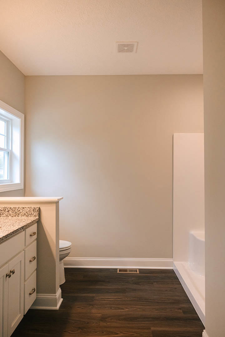 Modern bathroom featuring a white sink with chrome faucet, built-in vanity with light wood cabinetry, white toilet, neutral tile flooring, and a frosted window above the