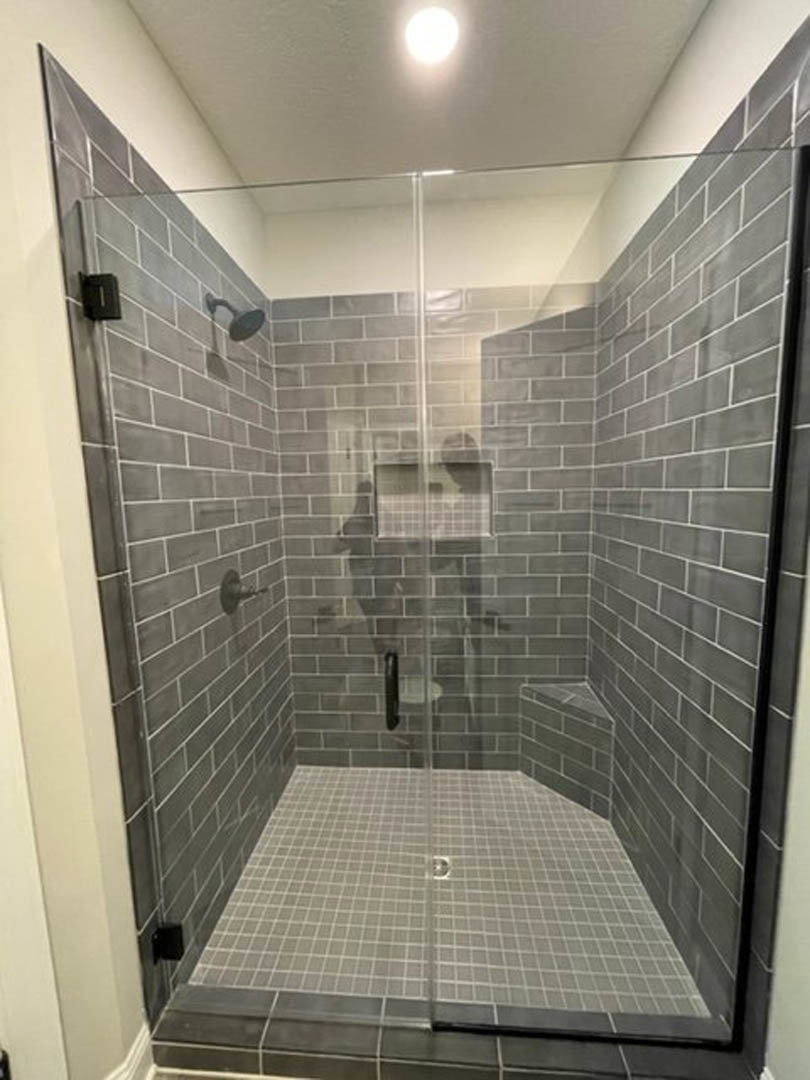 Shower with grey tile walls, glass door, chrome fixtures, and tiled floor in a modern bathroom
