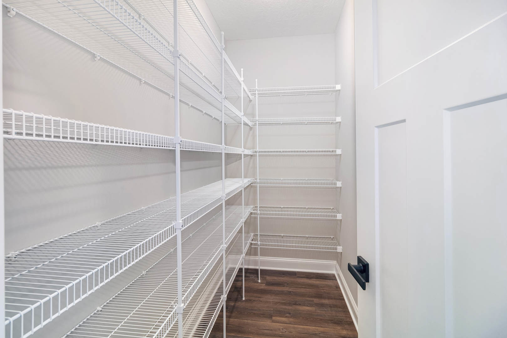 White built-in shelves with metal supports along a wall, light wood flooring, white baseboard trim, and a close-up of a modern door handle.