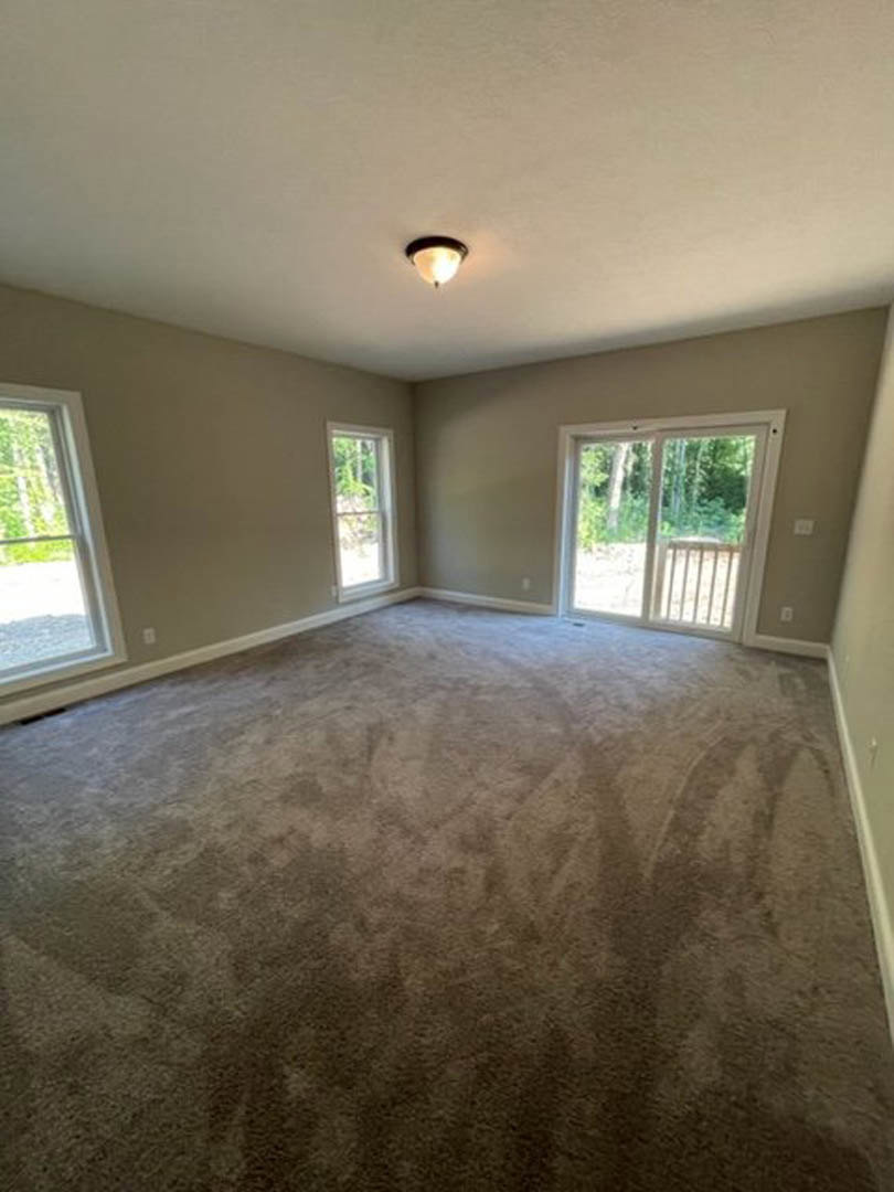 Sliding glass door and white-framed windows in a room with light-colored plaster walls, wood flooring, and ceiling-mounted light fixture