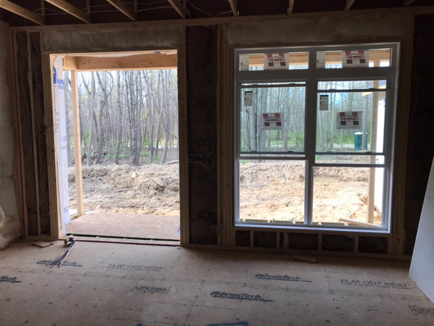 Spacious room featuring large wood-framed windows, glass door, light hardwood floors, and forest view through the windows.