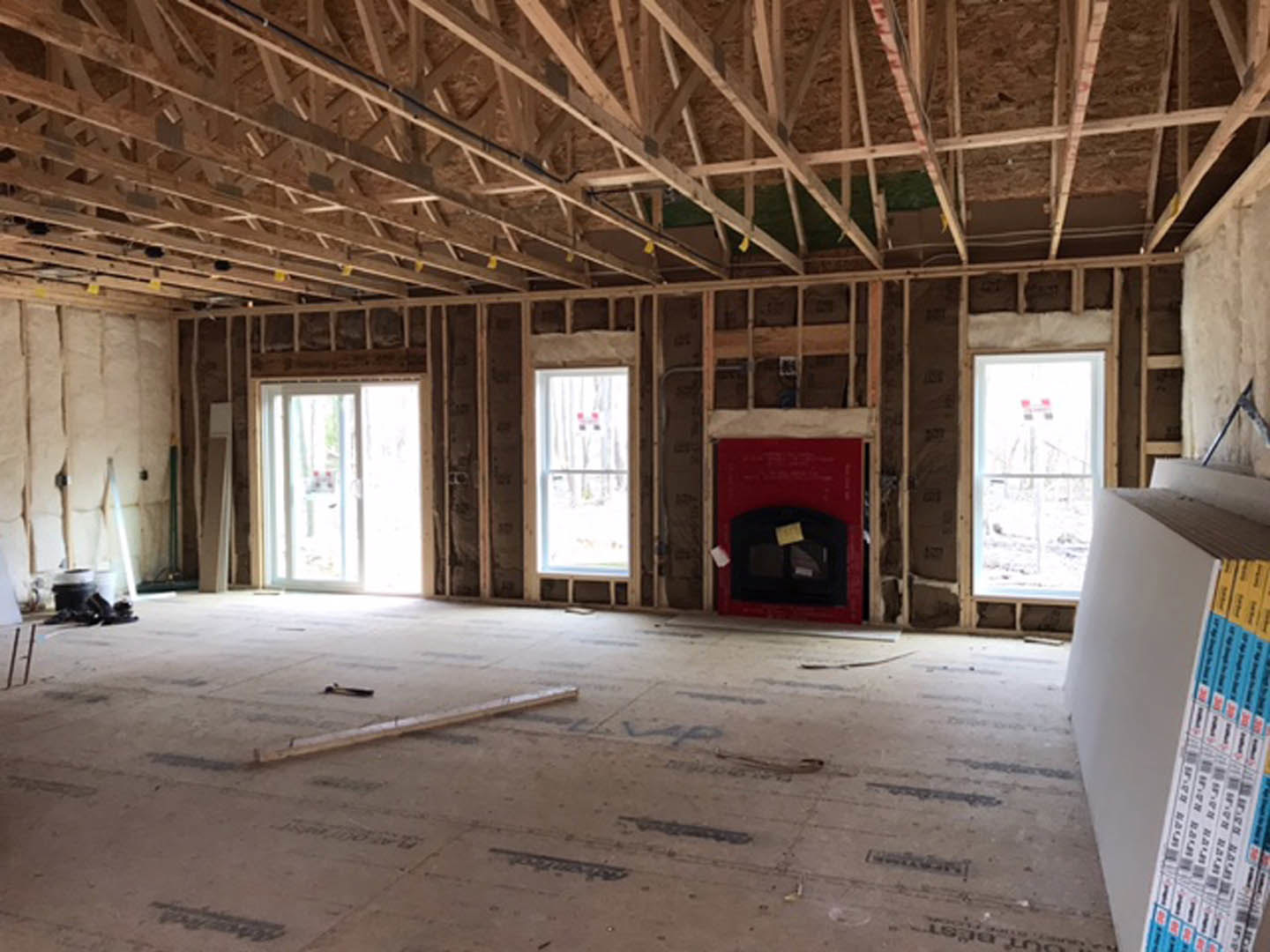 Exposed wood ceiling beams, unfinished walls, stone fireplace, large windows, construction materials scattered on floor