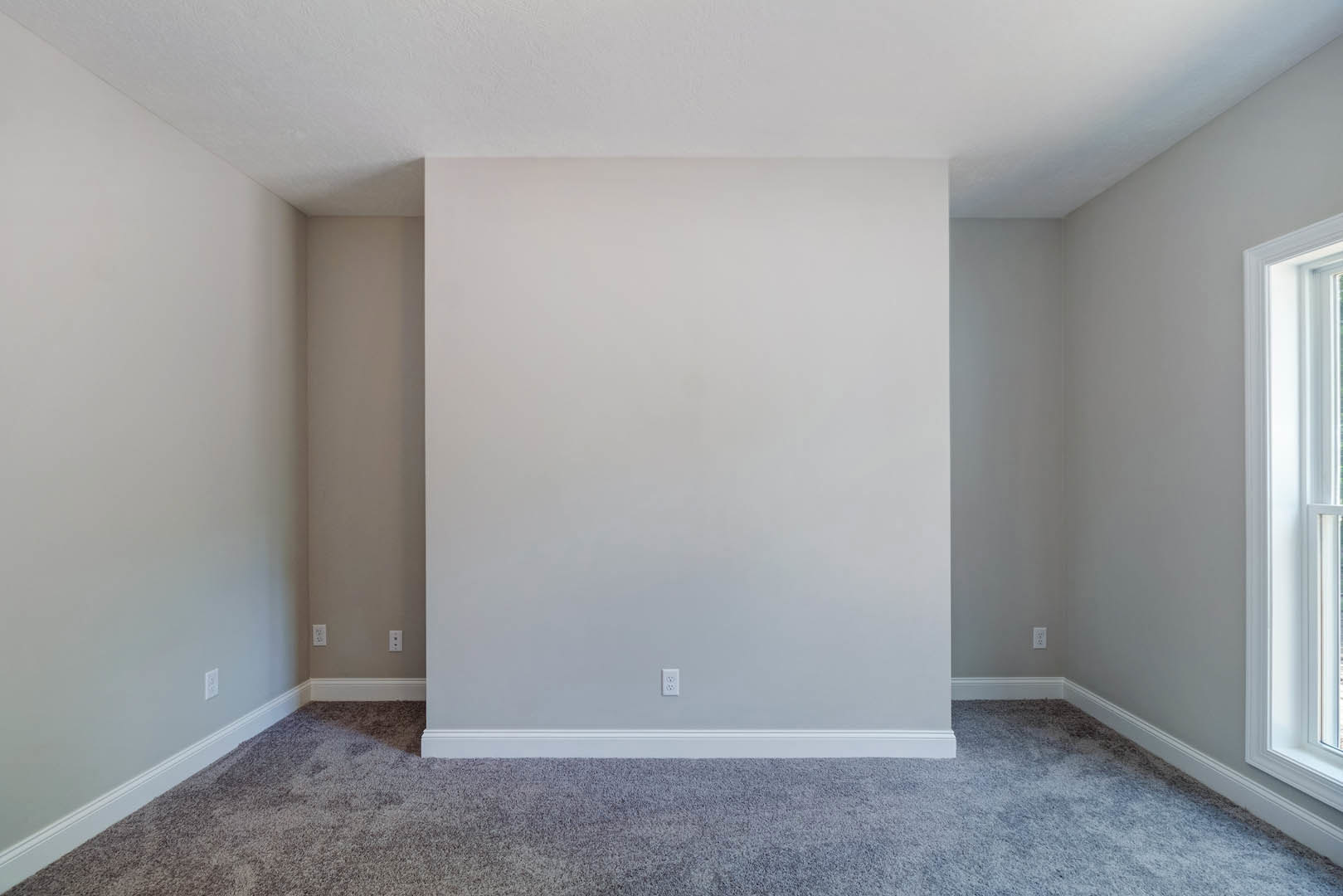 White carpeted floor, white plaster wall with baseboard molding, partial view of a window and door in a residential room.