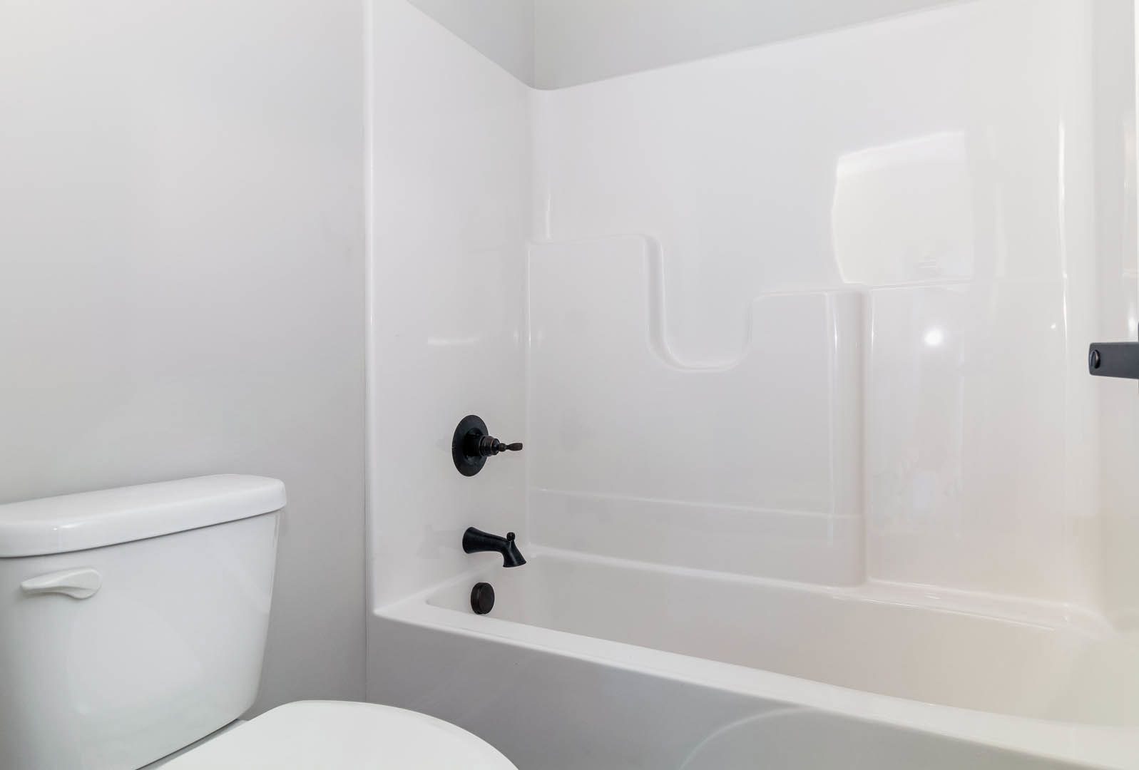 White bathroom with a freestanding tub featuring black fixtures, white tile walls, modern toilet, and minimalist finishes
