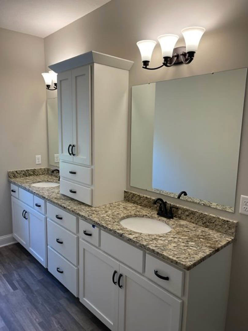 Bathroom with marble countertop, brown-bordered mirror, white cabinetry, chrome faucet, and tile backsplash.