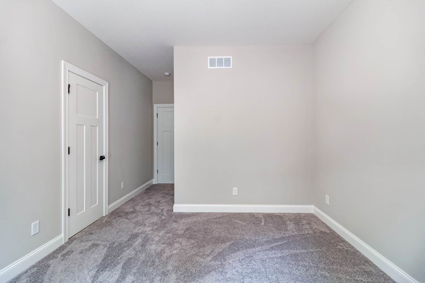 White paneled door with black handle, beige carpet flooring, white wall with air vent in a residential room