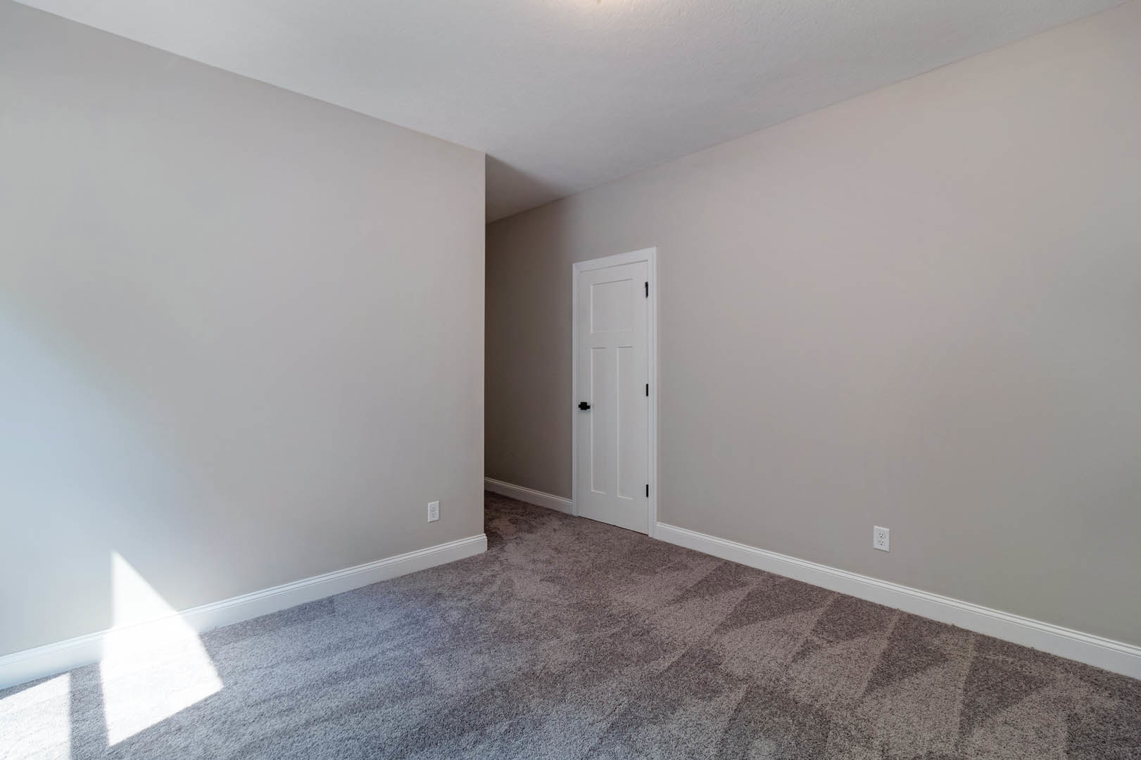 White carpeted floor, white walls, white ceiling with recessed light, white door featuring black handles, simple baseboard molding