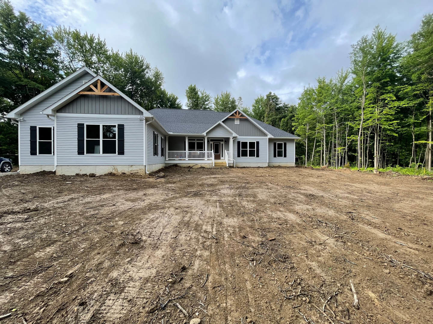 Two-story house with white-framed windows, white porch railing, dirt yard, and trees under a blue sky