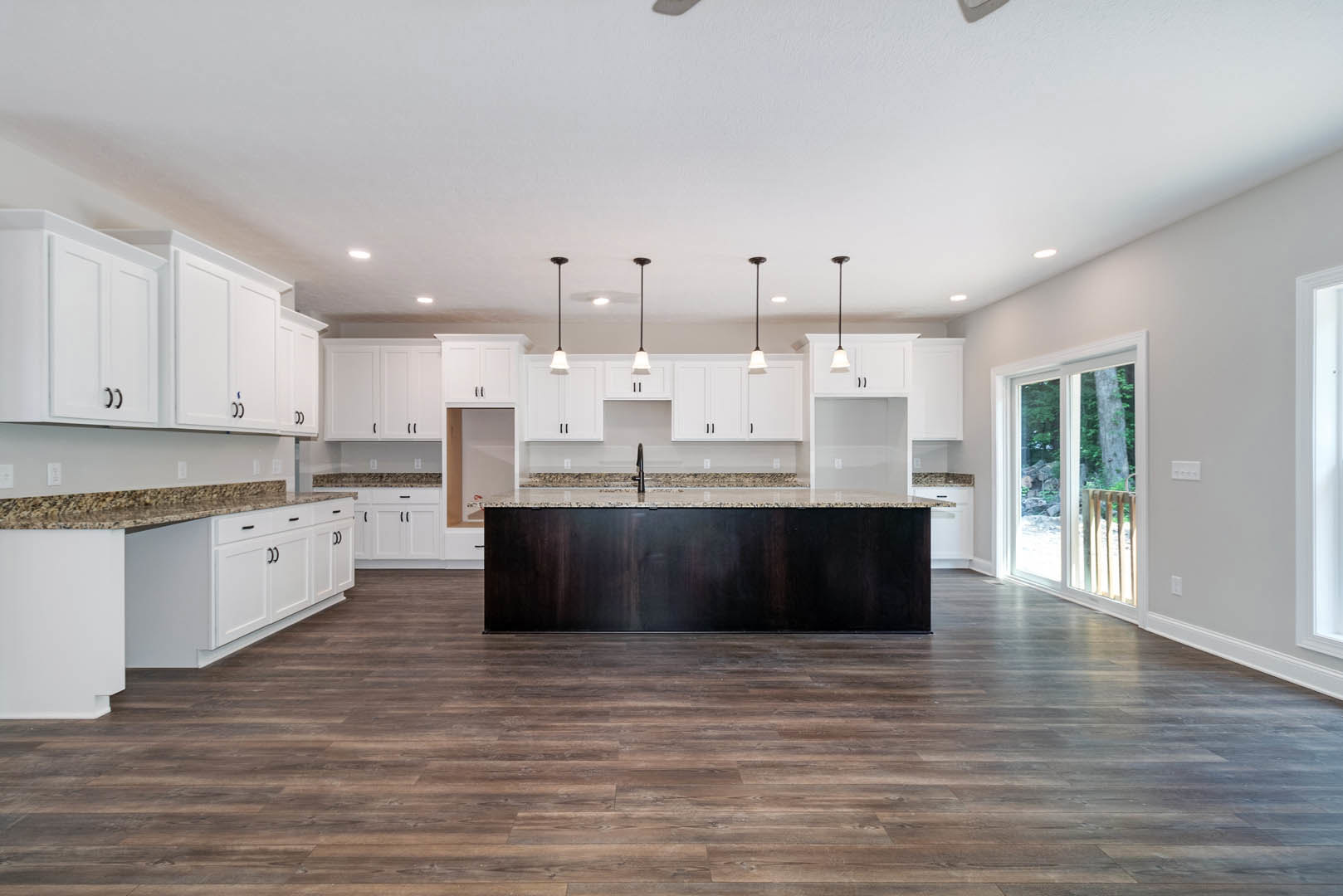 Spacious kitchen featuring a large white island with black accents, wood flooring, dark wall, white cabinetry with black handles, window with wooden trim, ceiling lights, and a