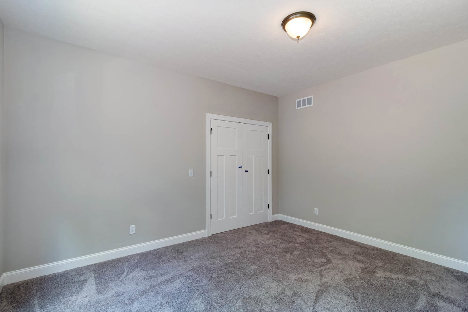 Carpeted bedroom with white closet door marked by blue tape, square window with white trim, ceiling light fixture, and neutral painted walls with crown molding.