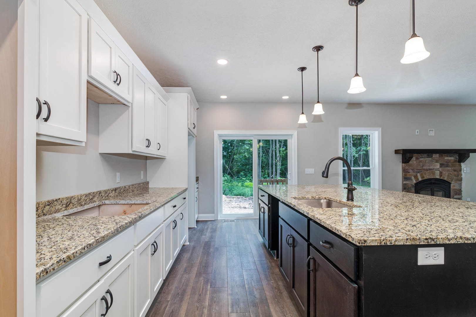 Kitchen with granite countertops, stainless steel sink, white cabinetry, kitchen island, stone accent wall, sliding glass door, pendant light fixtures with bell and white shades