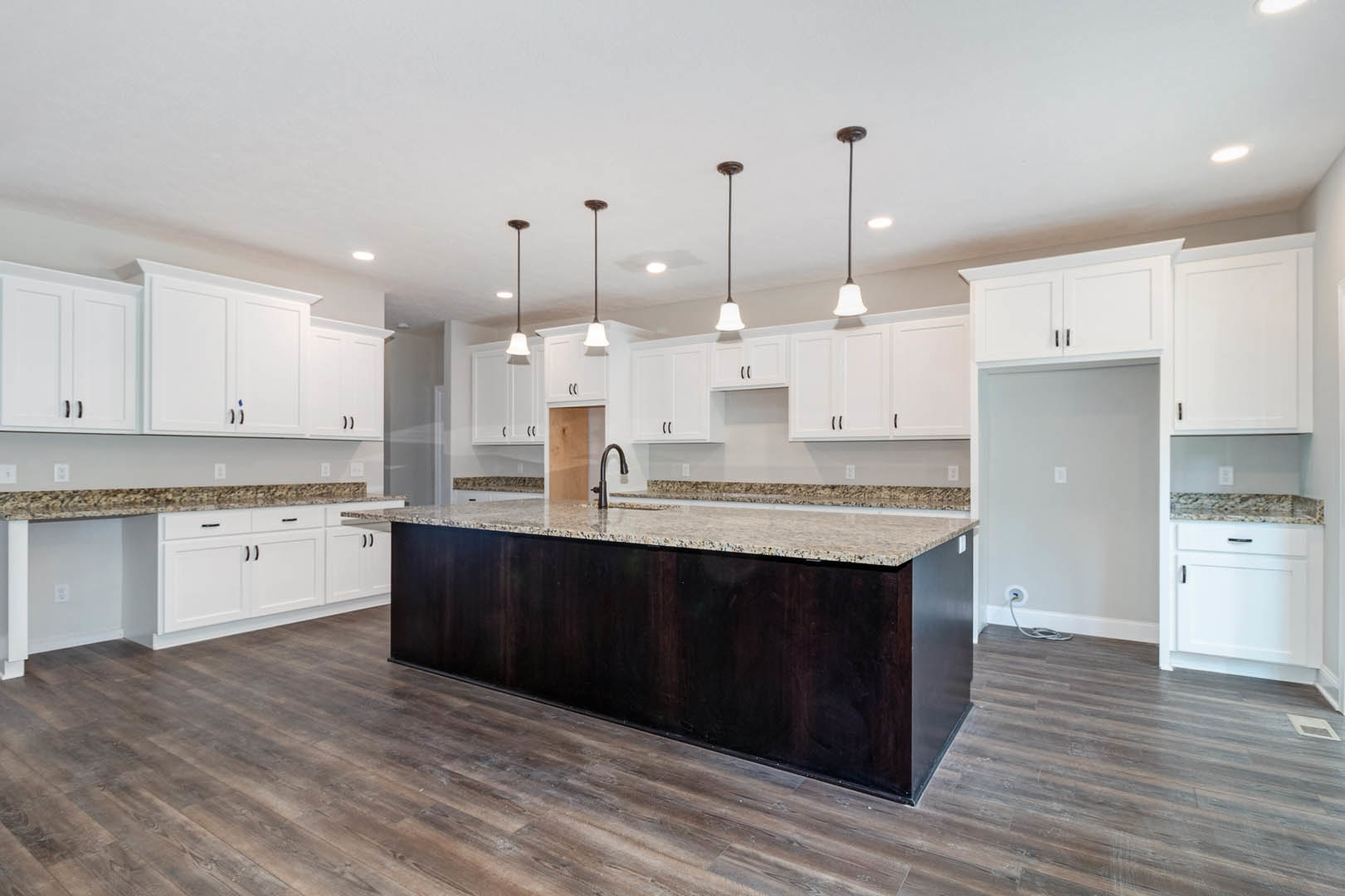 Spacious kitchen featuring a large granite island with built-in sink, wood flooring, white cabinetry, and stainless steel appliances.