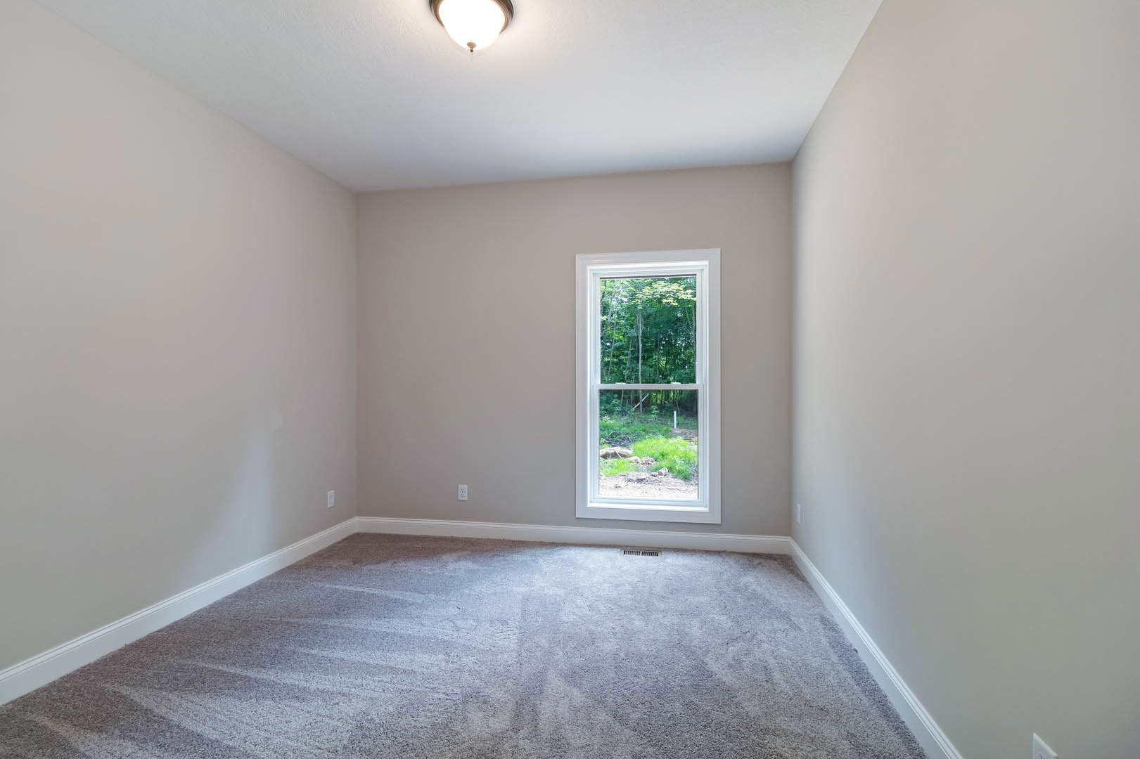 Carpeted bedroom with large window overlooking trees, white walls, ceiling light fixture, and decorative molding