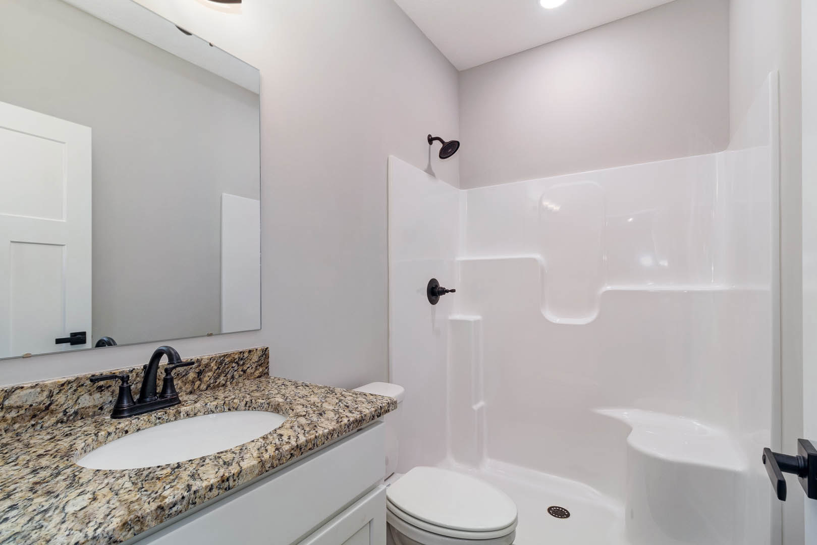 Marble countertop with black faucet, white undermount sink, glass-enclosed shower with tile walls, and white toilet adjacent to paneled door