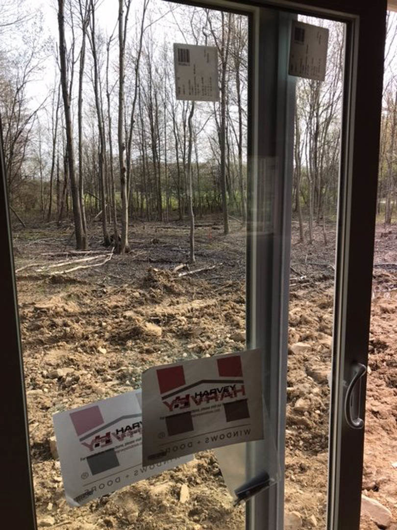 Large window with white trim overlooking a dirt field and cluster of trees, natural light streaming into interior space