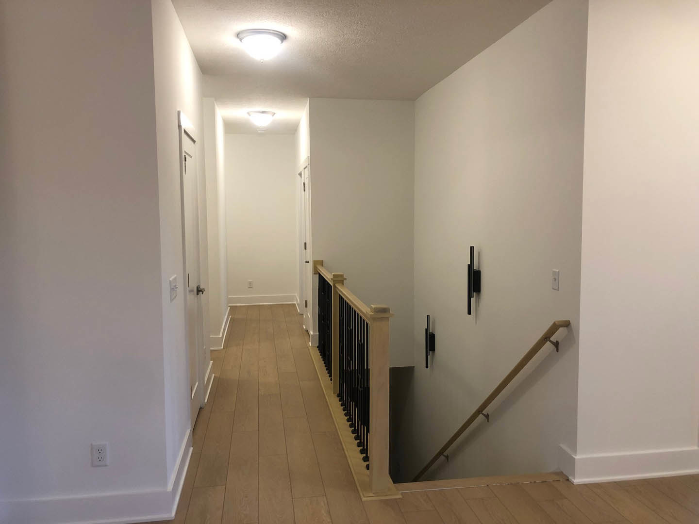 Hallway with wood flooring, white plaster walls, staircase featuring a metal handrail, modern light fixture, and a light switch on the wall