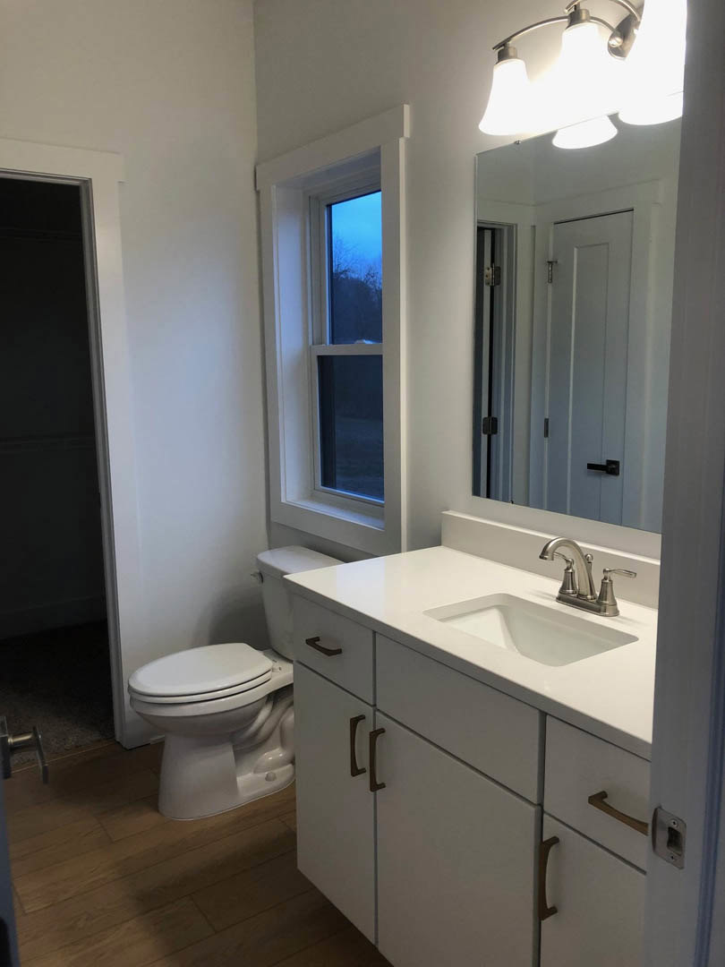 Modern bathroom with white toilet, rectangular sink on stone countertop, black door with white trim, light fixture above, and neutral tile walls