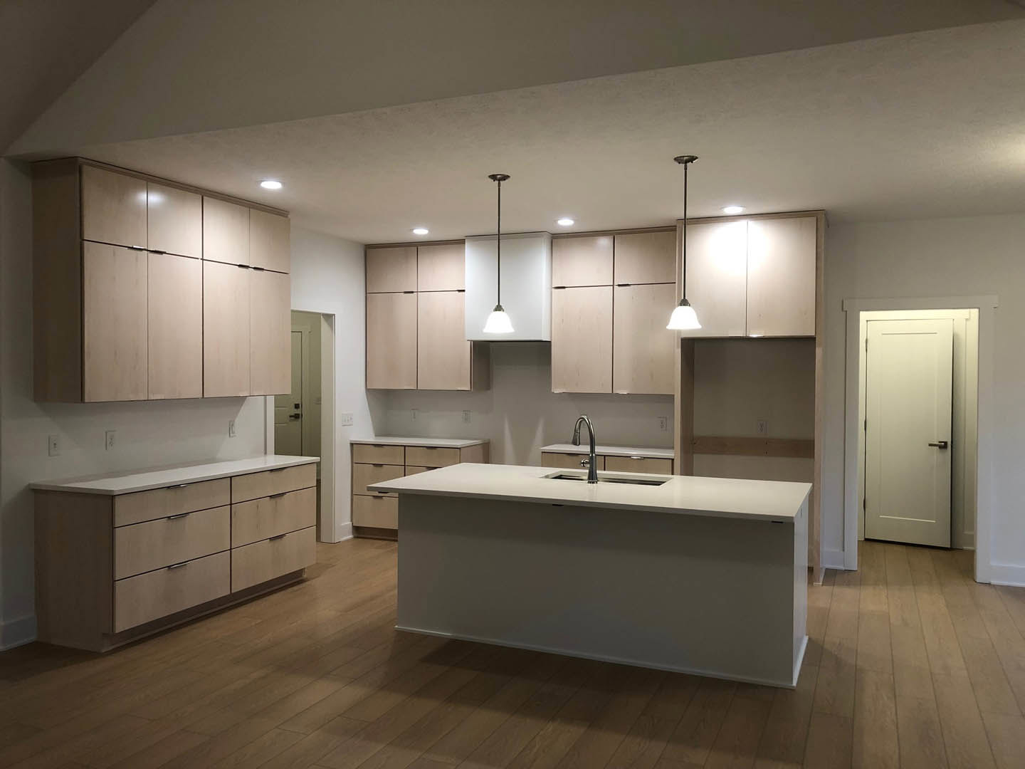 Kitchen featuring a white island with waterfall countertop, wooden base cabinets, stainless steel faucet, tile backsplash, and white paneled door with silver handle
