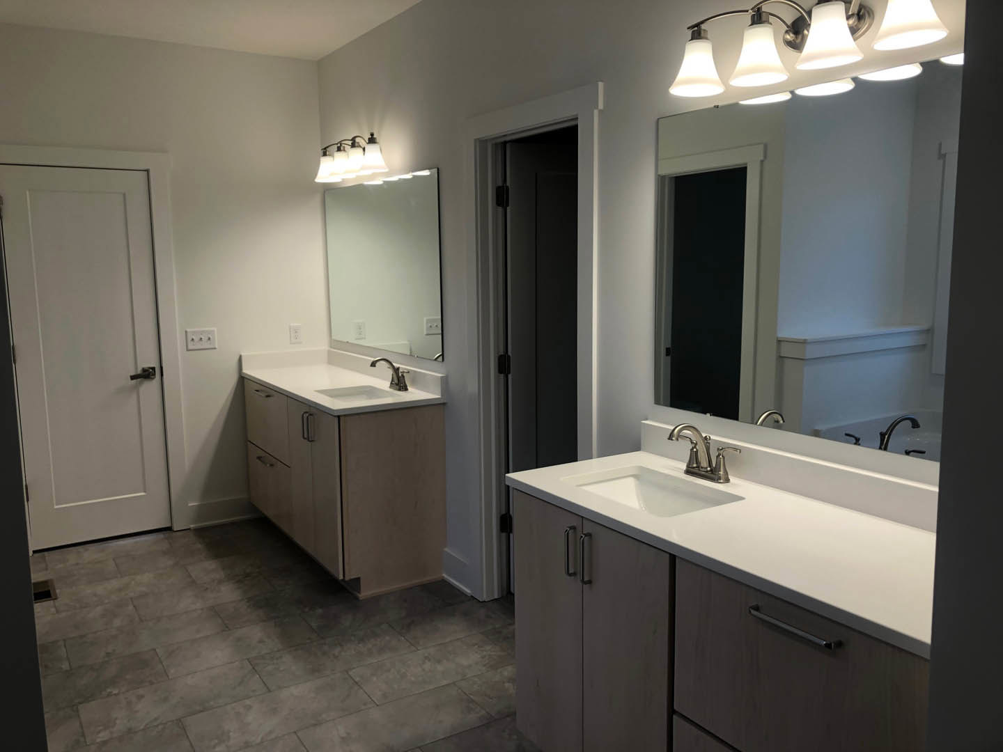 Double vanity with two rectangular mirrors above, white cabinetry, chrome faucets, grey tile flooring, white walls, and a white door with silver handle