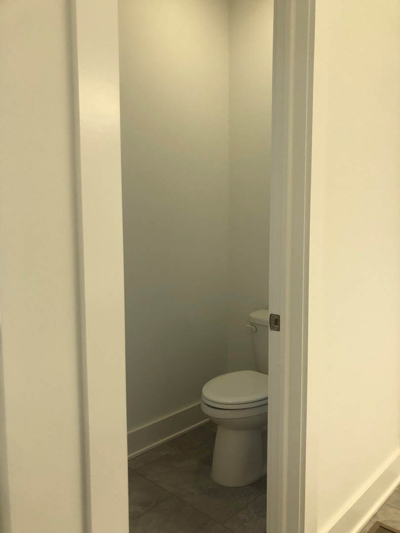 White toilet with closed lid against a white wall, gray tile flooring, and partial view of bathroom door
