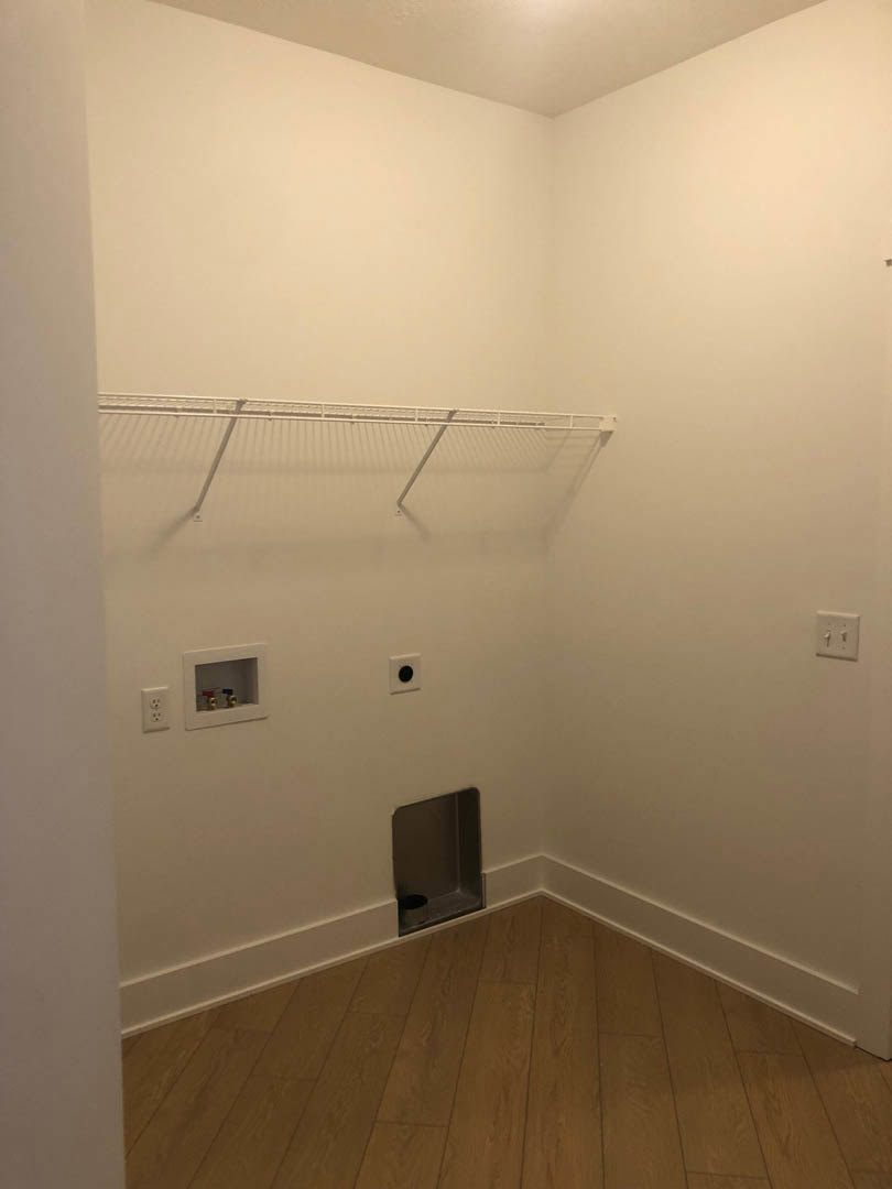 White plaster wall with a metal rack mounted above a wood floor, light switch visible nearby, small hole in wall below the rack.