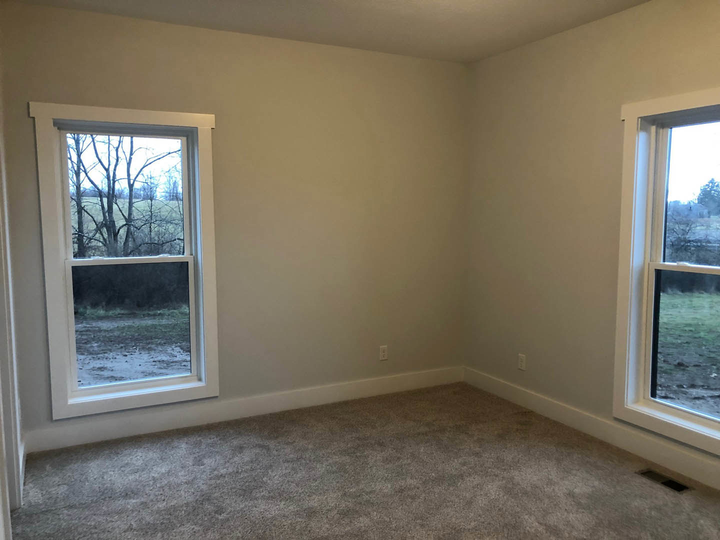 Carpeted room with white baseboards, large window overlooking grassy field and trees