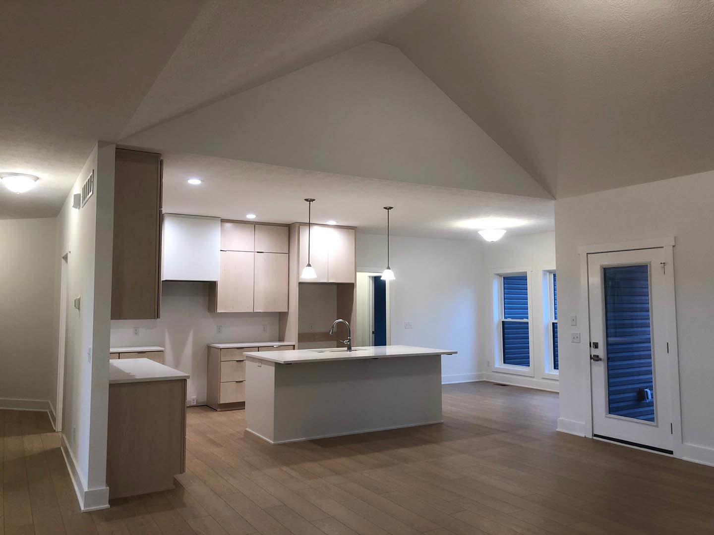 Open kitchen and dining area featuring a white island with integrated sink and faucet, wood flooring, white cabinetry, and a wall with a white-framed door.