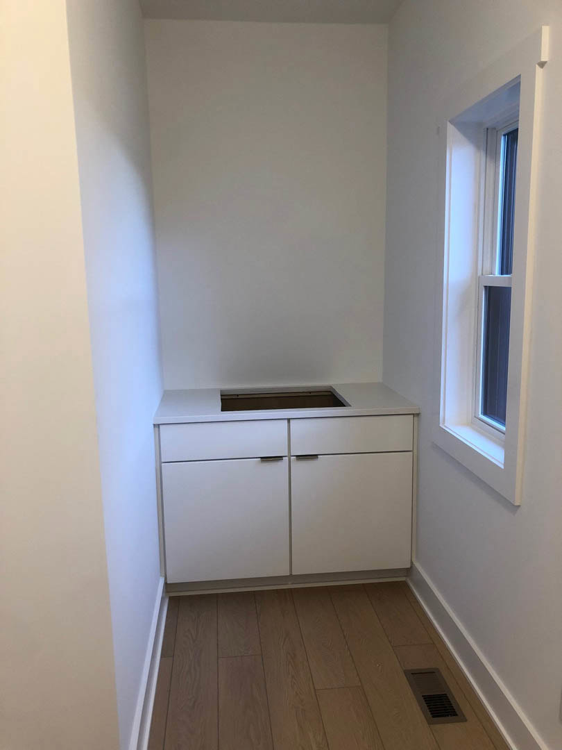 White kitchen cabinet with silver handles, wood floor, wall vent, and nearby window.
