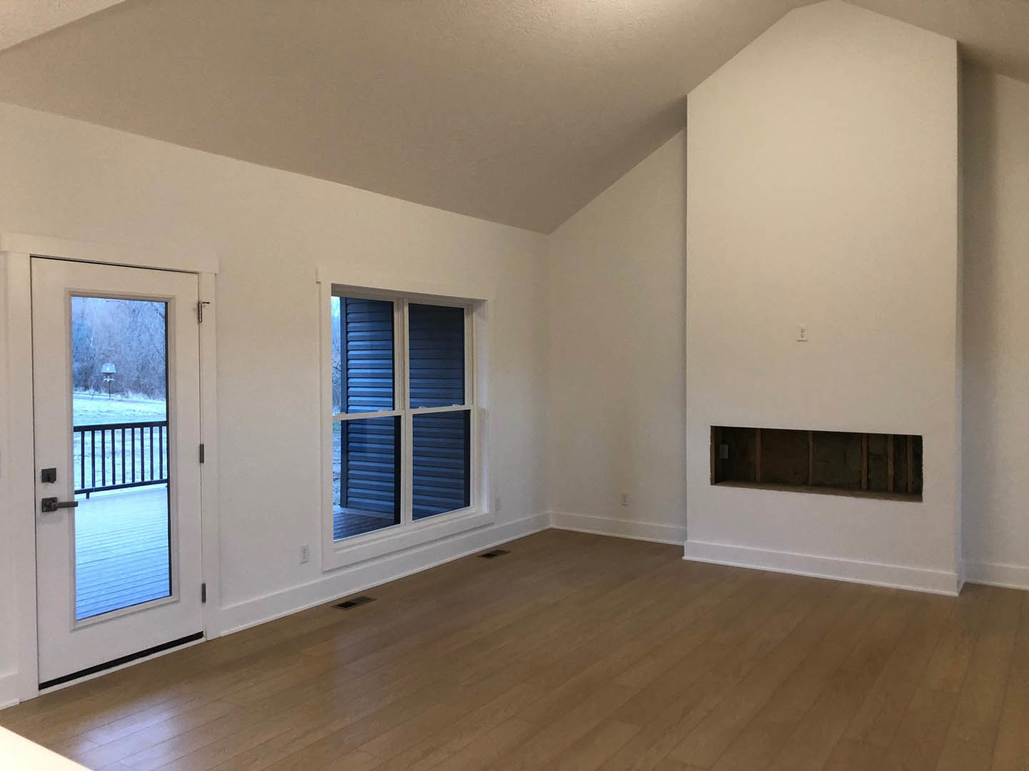 Wood flooring in a room with white plaster walls, a multi-pane window, and a door opening to a snowy landscape