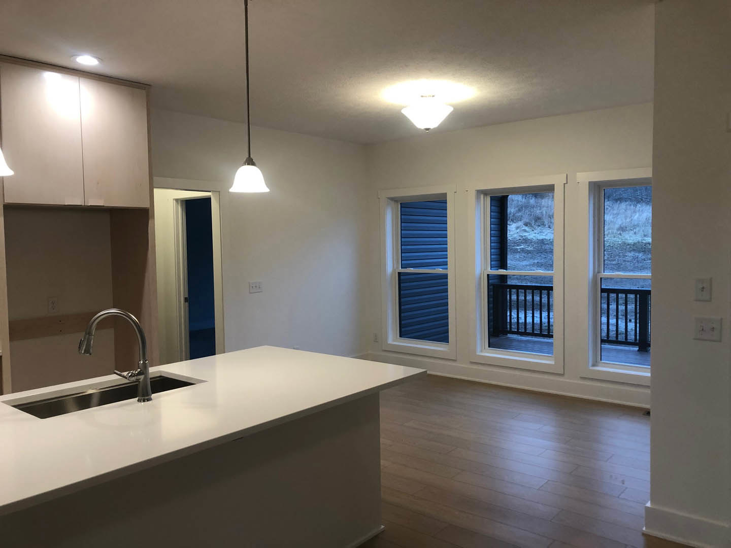 Modern kitchen featuring a white countertop bar with built-in faucet, large windows with white frames, light fixture on ceiling, and tiled walls.