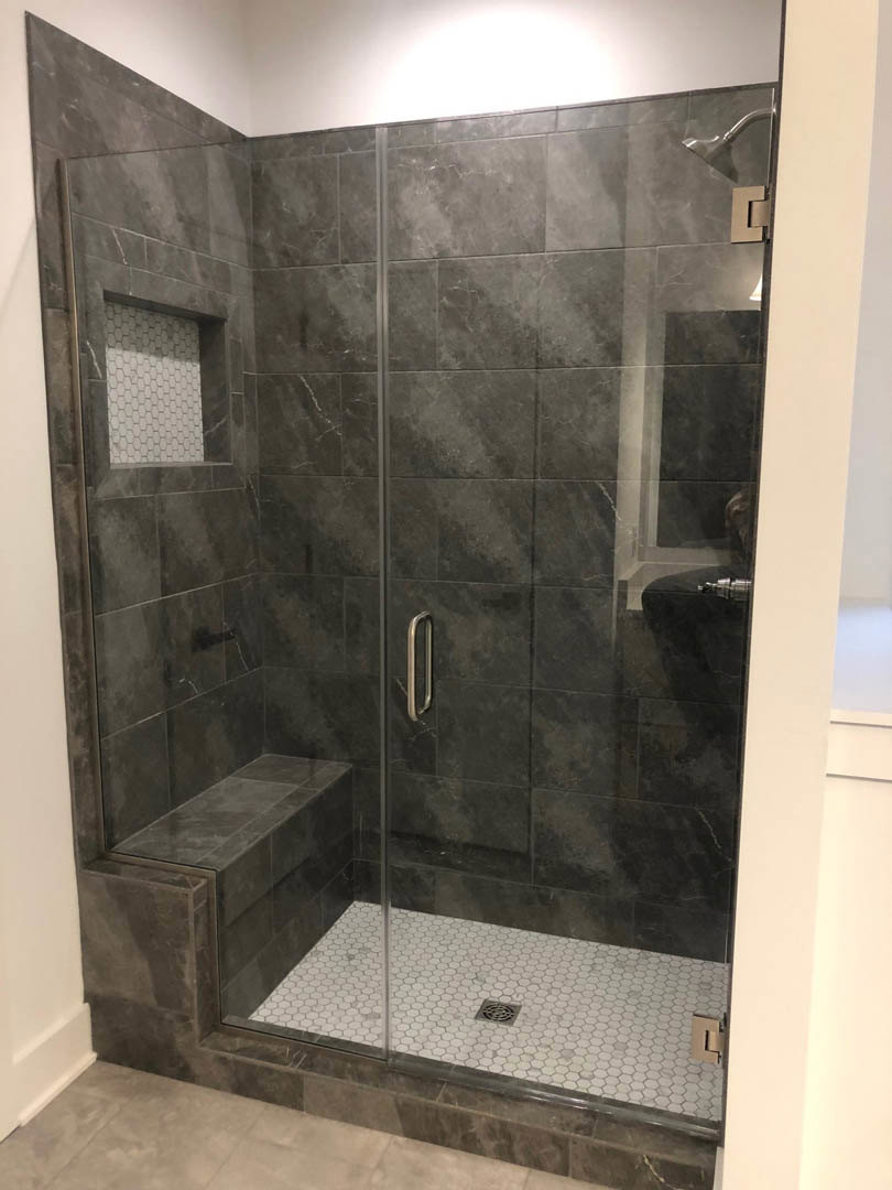 Glass shower enclosure with built-in grey tile bench, white tile walls, tile flooring, and chrome faucet visible