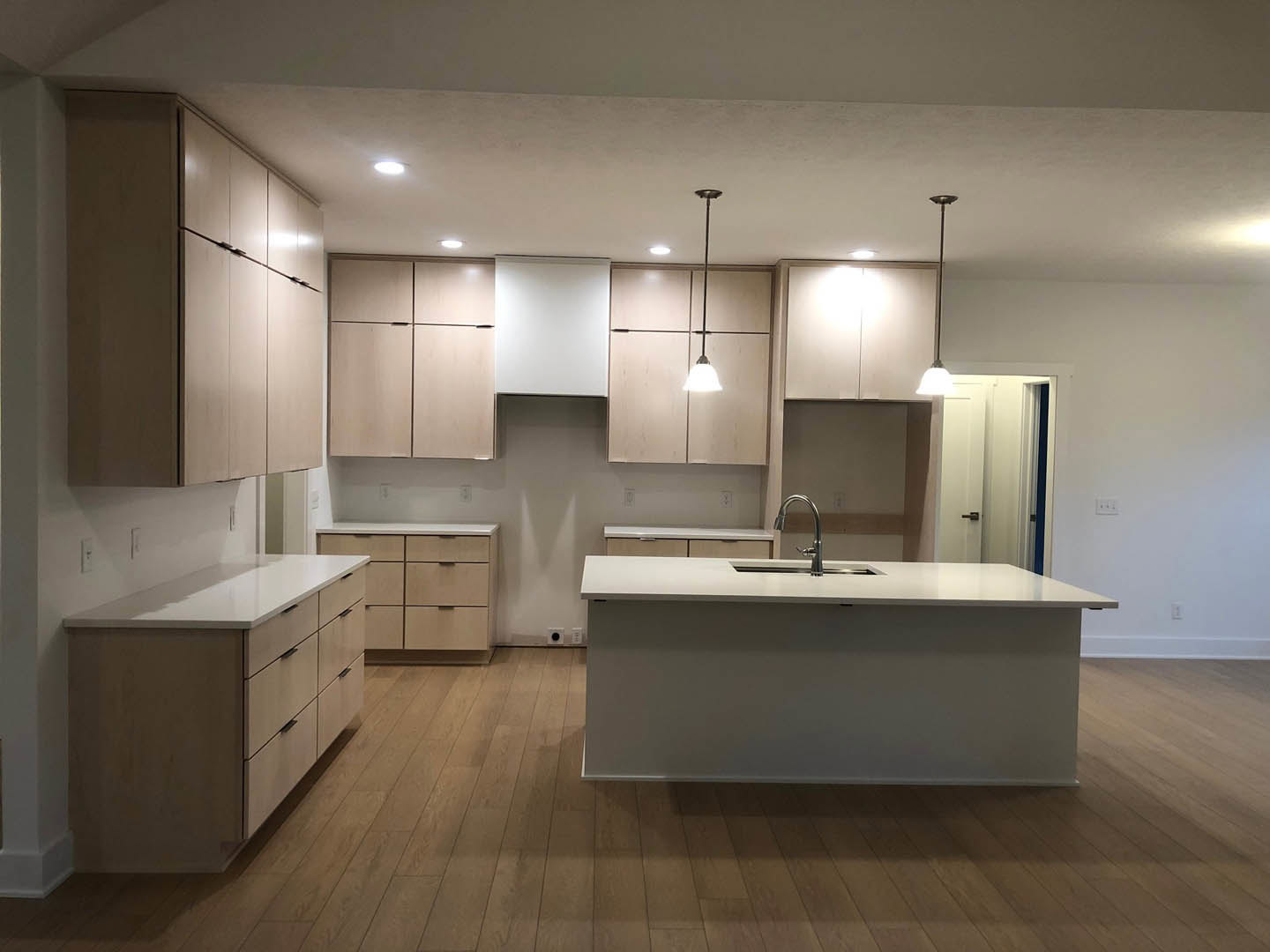 Spacious kitchen featuring a large white island with built-in sink, white cabinetry, wood flooring, and a contrasting black door against white walls