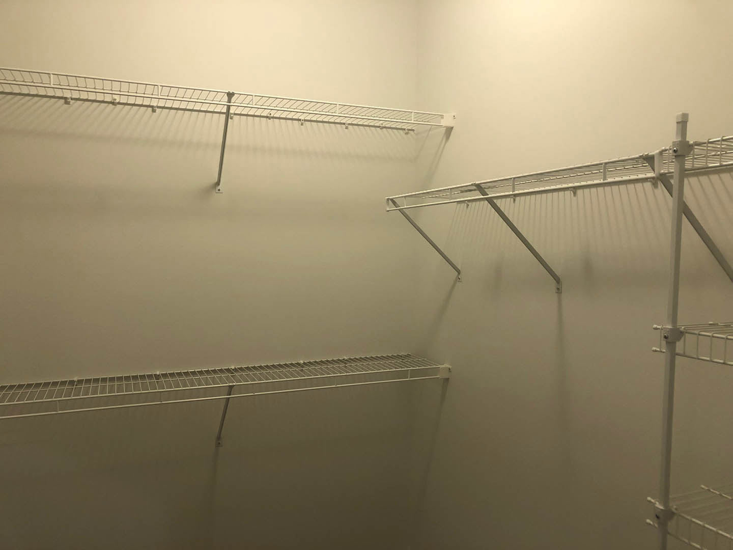 White closet corner with metal shelving and hanging rod, white shelf mounted above smooth wall, steel finishes throughout.