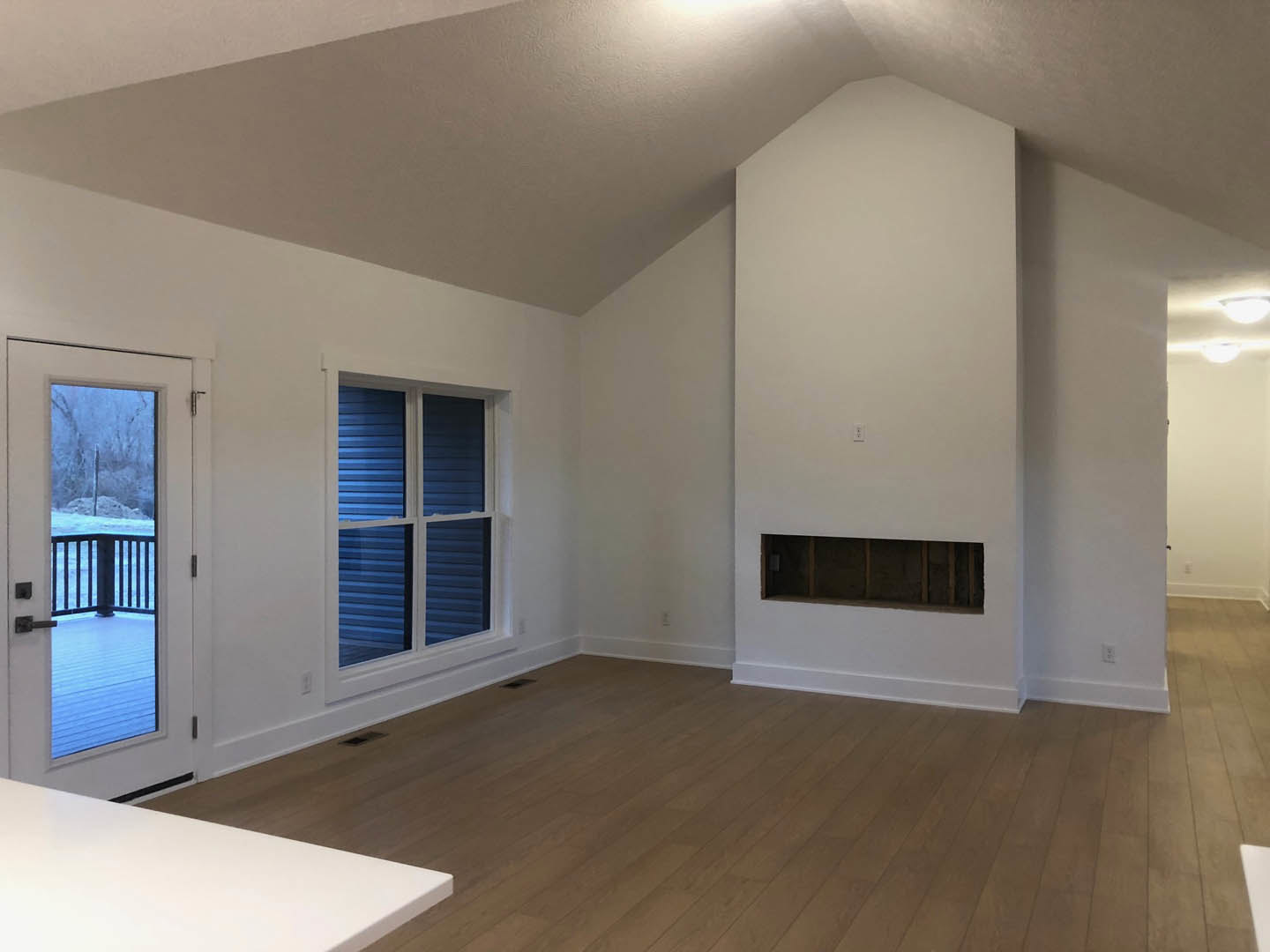Wood flooring and white plaster walls, white table near window, door opening to snowy landscape, electrical outlet on wall