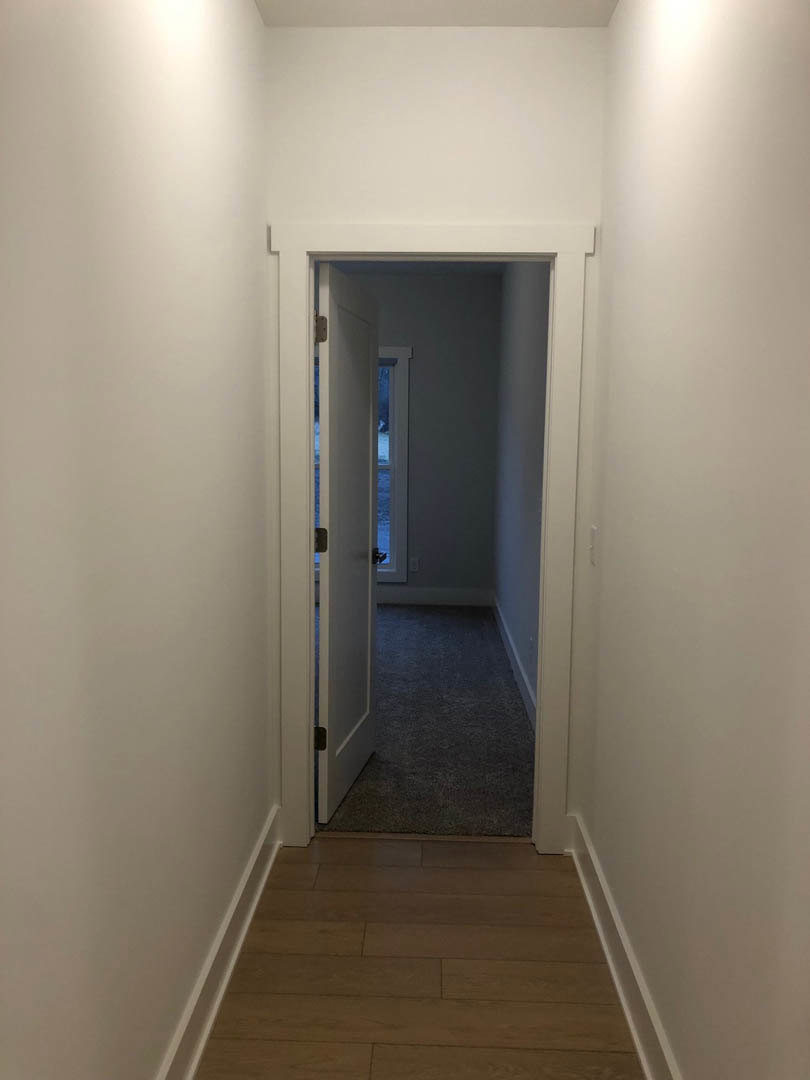 White hallway with wood flooring, open white door leading to a room, smooth plaster walls, ceiling with recessed lighting