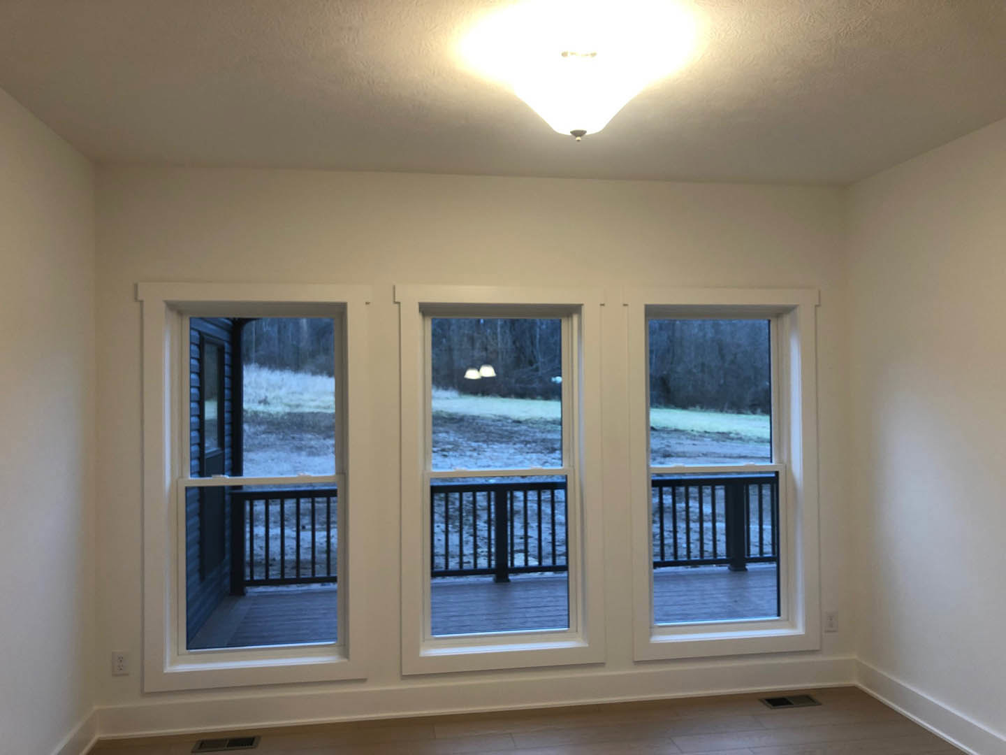 Open living area with large windows, white tile flooring, modern light fixture, sliding door to deck with metal railing, snowy landscape and trees visible outside