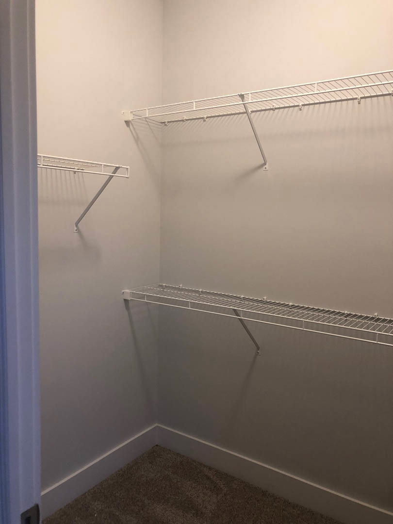 Walk-in closet featuring white built-in shelves, white walls, and light carpet flooring