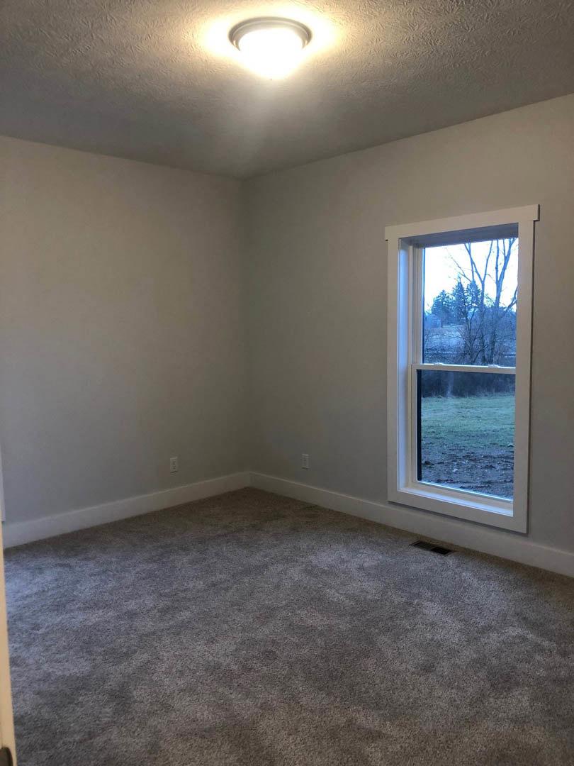 Carpeted bedroom with white walls, large window overlooking grassy field and trees, round ceiling light fixture