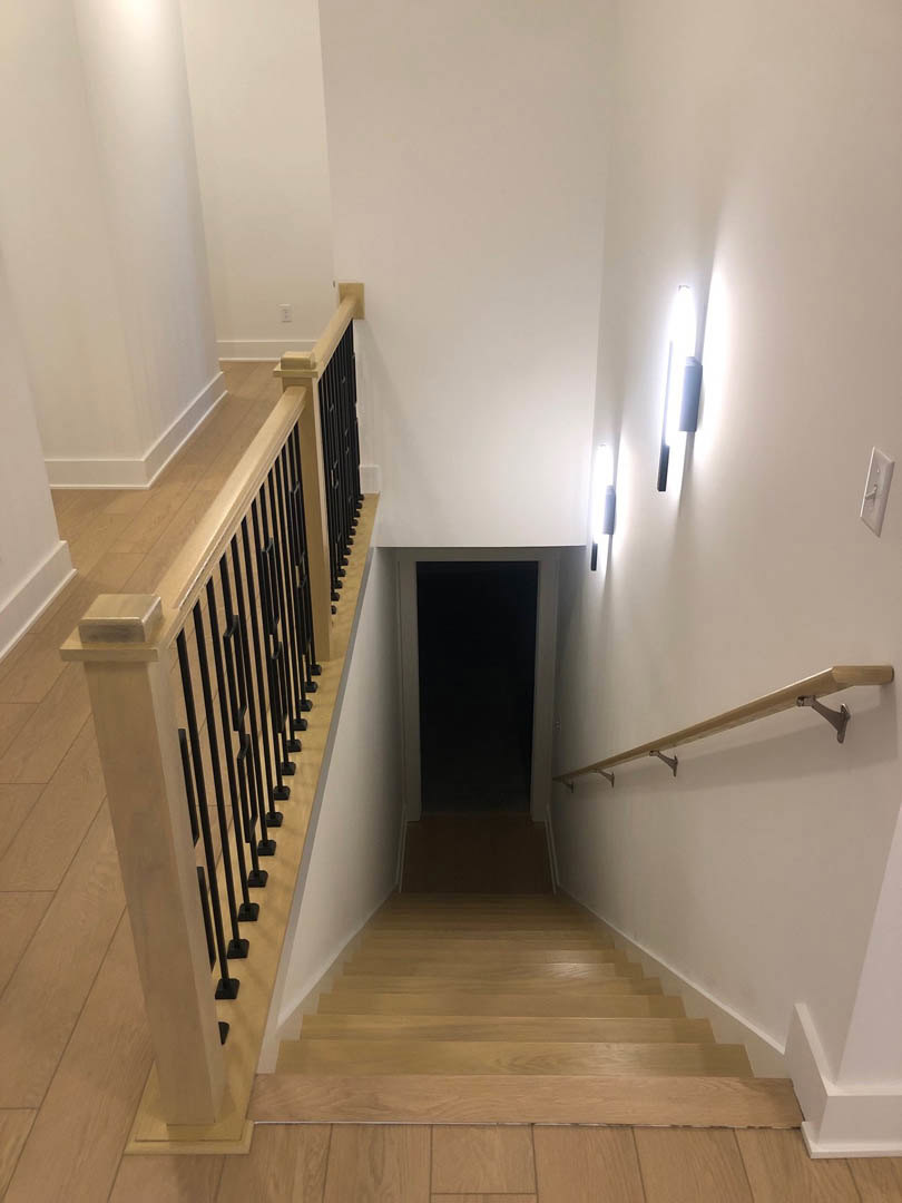 Wooden staircase with white plaster walls, black metal handrail, and a white-framed door at the landing