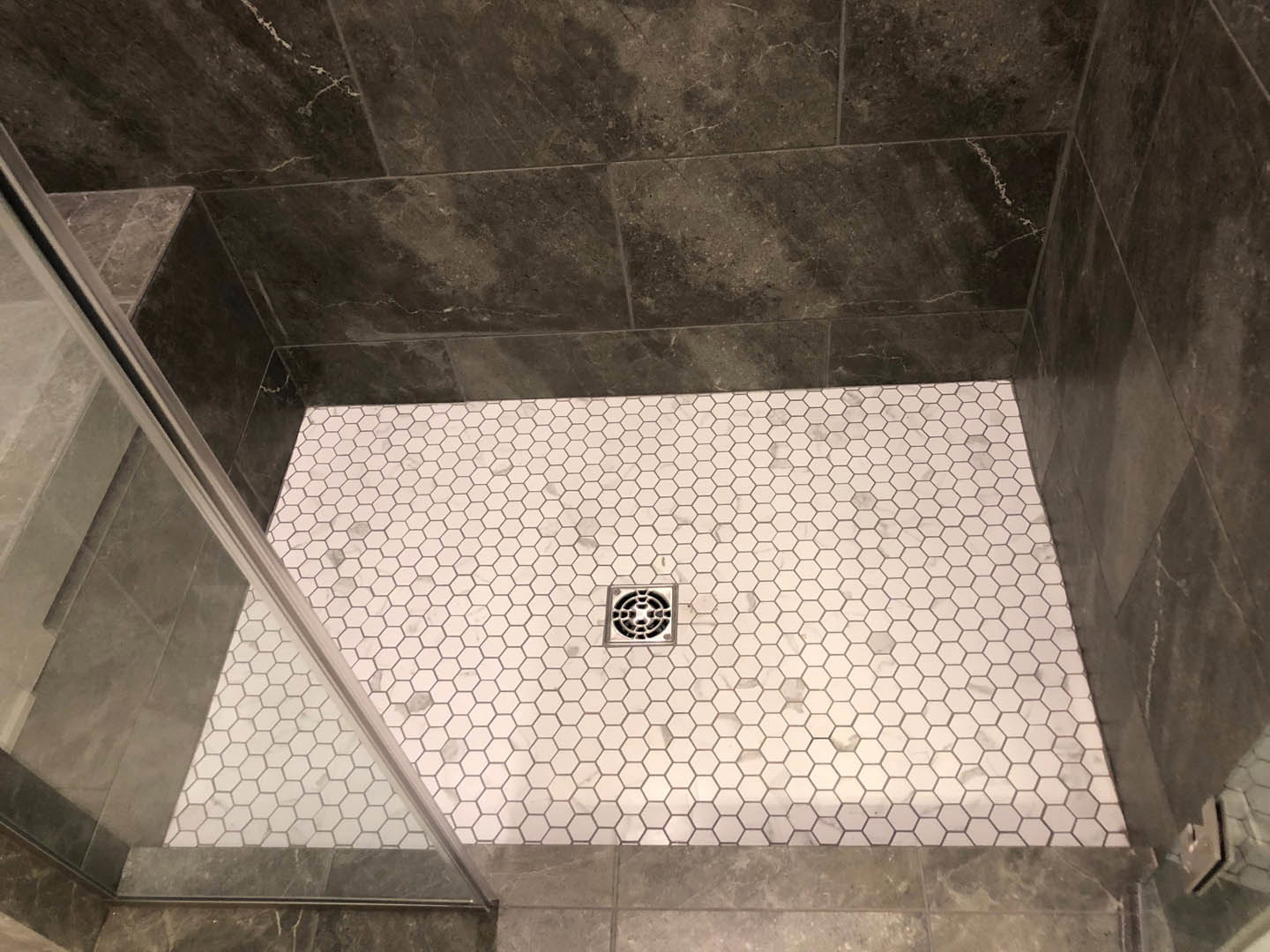 Walk-in shower with glass door, white tile walls and floor, linear drain, chrome fixtures, and marble accent tiles