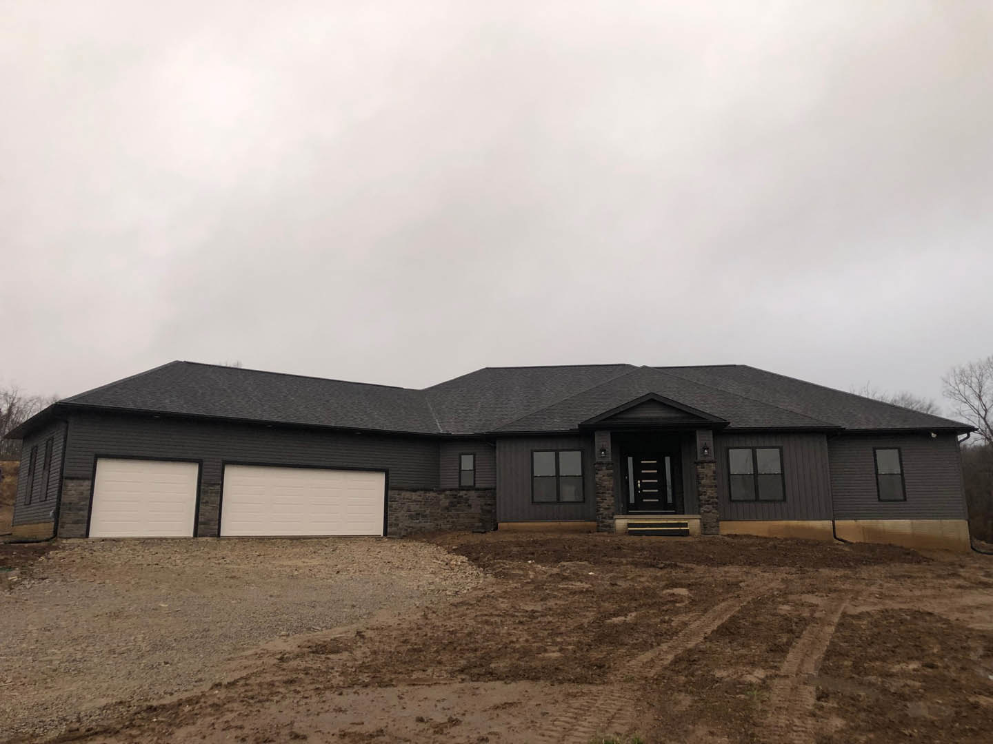 White two-story house with black trim, attached garage with white door, concrete driveway, large front window, manicured lawn, and overcast sky.