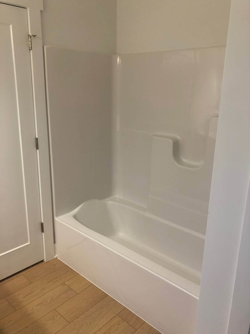 Freestanding white bathtub on light wooden floor, white plaster walls, minimalist bathroom with chrome tap and subtle tile accents