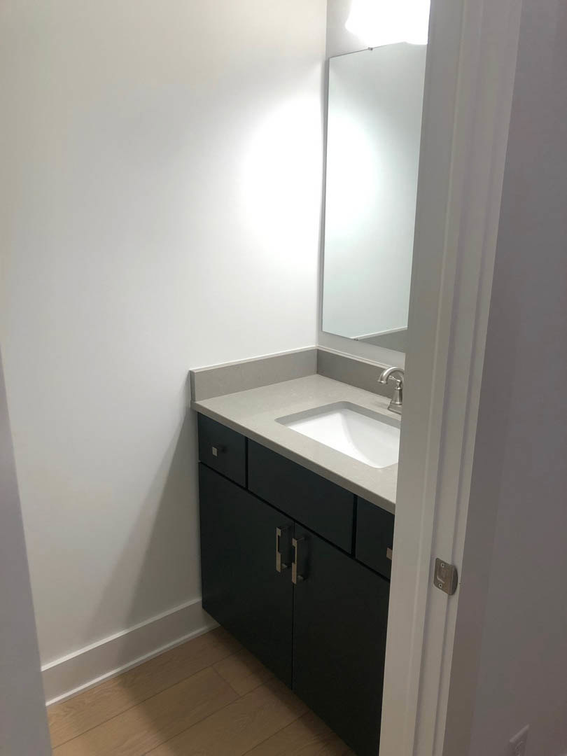 Triangular white sink set in a black cabinet, rectangular mirror above, white walls with black border, wood flooring with white trim